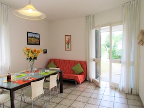 A dining area with a table, chairs, a vase of flowers, and a sofa with cushions.