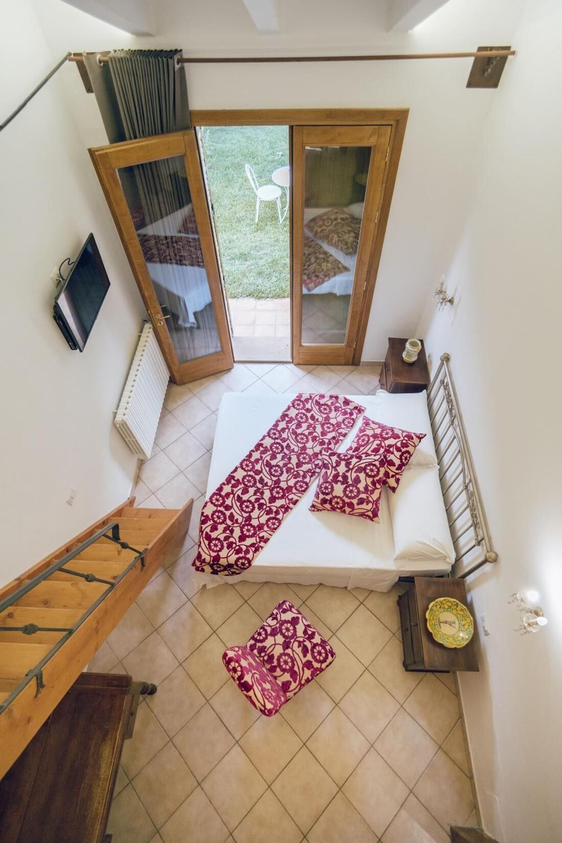 Un dormitorio con una cama, un escritorio de madera, un radiador y un ventanal corredera a un balcón.
