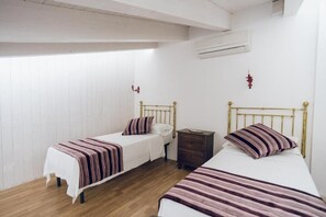 A small, clean room with two single beds, a wooden floor, white walls, and a simple air conditioning unit. - Leano Agriresort - Superior Triple Room With Mezzanine (Piazza Armerina)