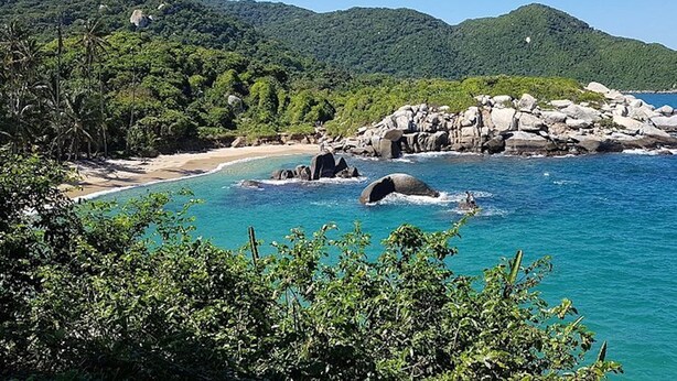 Un paysage côtier avec une plage, des eaux d’un bleu limpide et des formations rocheuses.