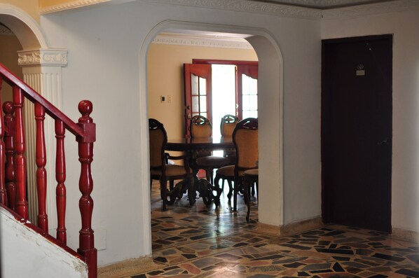 A dining area with a table and chairs, a staircase with red balusters, and a patterned floor.