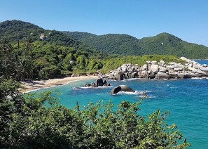 A coastal landscape with a beach, clear blue waters, and rocky formations. - Hostal Hogar Buenaventura (Santa Marta)