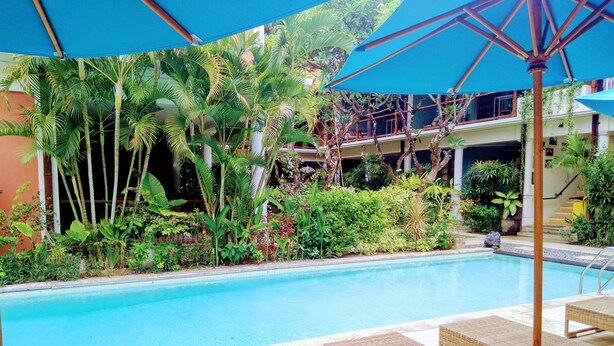 A pool area with lounge chairs and umbrellas, surrounded by lush greenery and a building in the background. - 2 Bedrooms Vintage Apartment 10 - Balcony,private Kitchen,livingroom,pool (Legian)