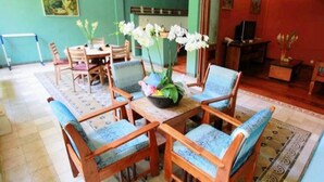A room with a dining table surrounded by four wooden chairs with blue cushions, a vase with white flowers, and a television on a wooden cabinet. - 2 Bedrooms Vintage Apartment 10 - Balcony,private Kitchen,livingroom,pool (Legian)