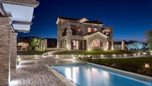 Une grande maison en pierre à plusieurs étages, avec une piscine en premier plan.