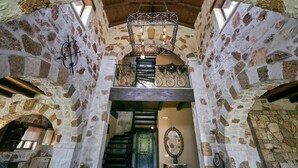 Un intérieur aux murs de pierre, agrémenté d’un escalier, d’un lustre et d’un miroir.
