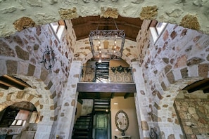 A stone-walled interior with a staircase, a chandelier, and a mirror. - Palazzo Di P Villa, Zakynthos Exclusive Private Villa With Pool (Zakynthos)
