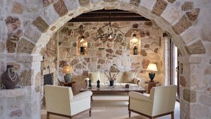 Une pièce aux murs de pierre, dotée d’un haut plafond en arc de cercle, d’un canapé, de deux fauteuils, d’une table basse et de lampes fixées au mur.