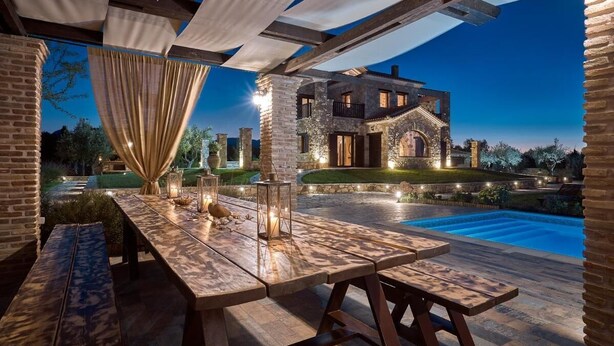 Une terrasse extérieure avec une piscine, un bâtiment en pierre et une table en bois décorée de lanternes.