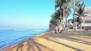 A beach with palm trees, a sandy shore, and a building with a sign in a foreign language.