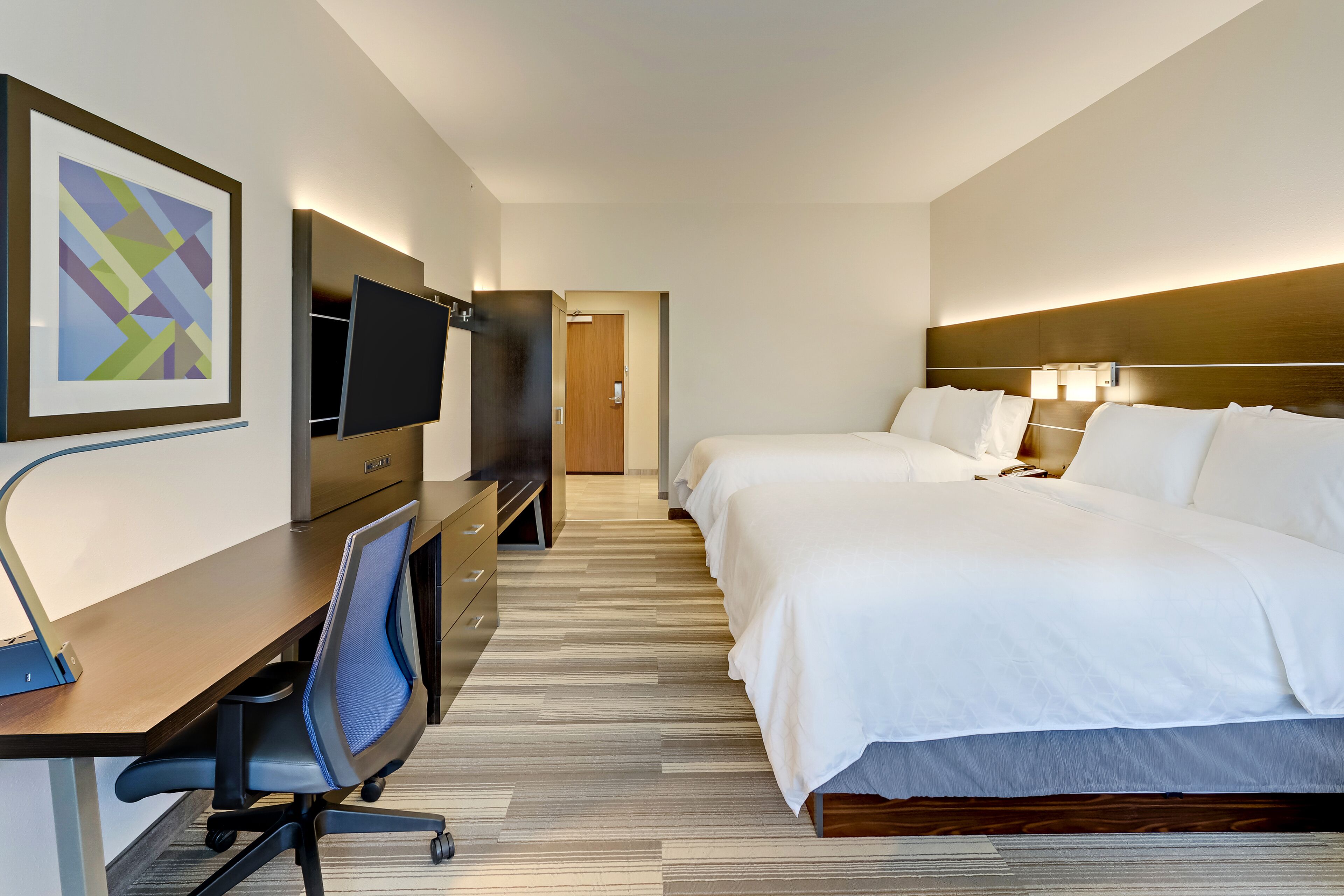 A hotel room with a desk, two beds, a TV, and a framed picture on the wall.