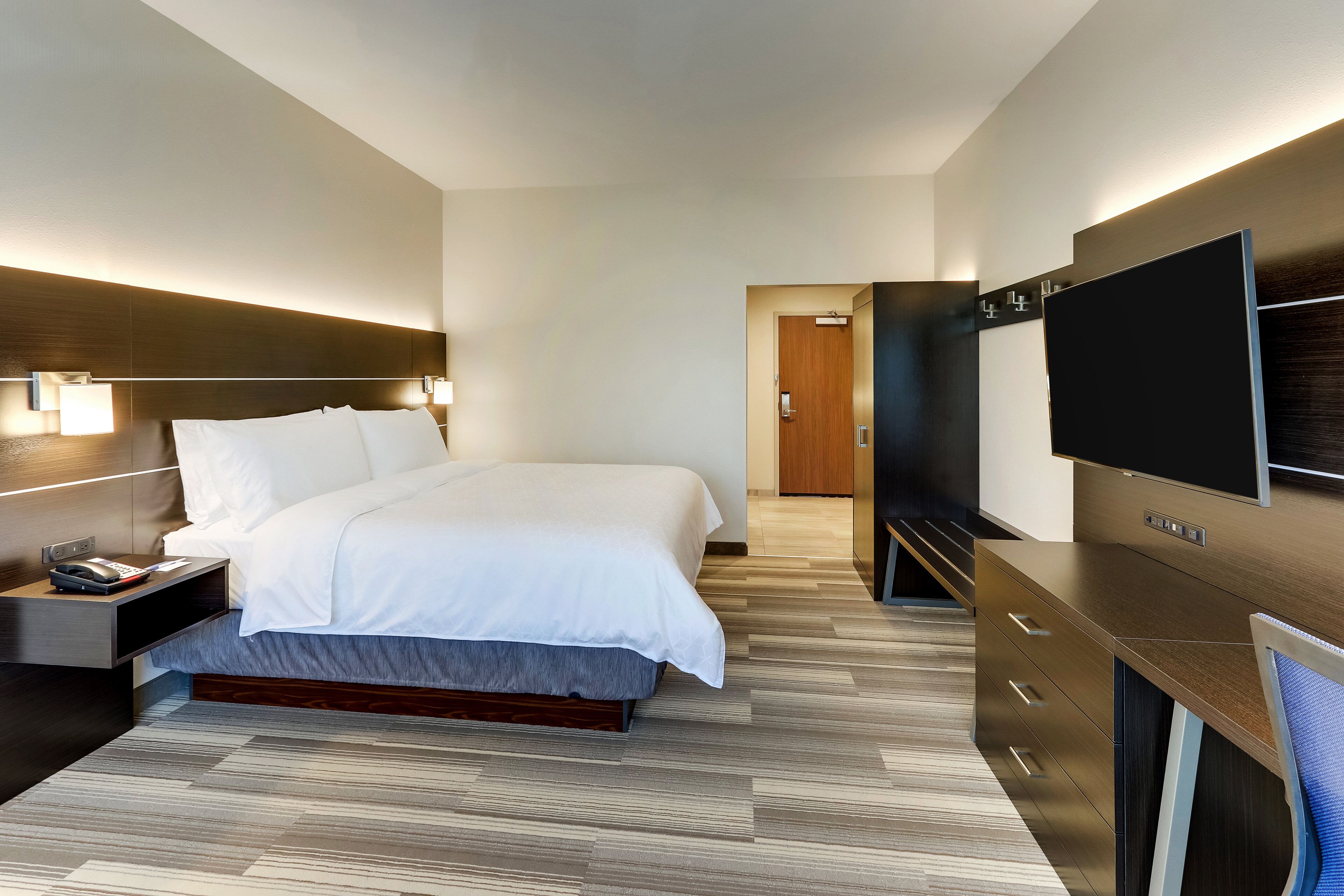 A modern hotel room with a large bed, bedside tables, a TV, and a wooden floor.