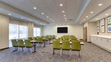 Une salle de conférence avec des chaises, des tables et un grand écran, le tout dans des tons de vert.