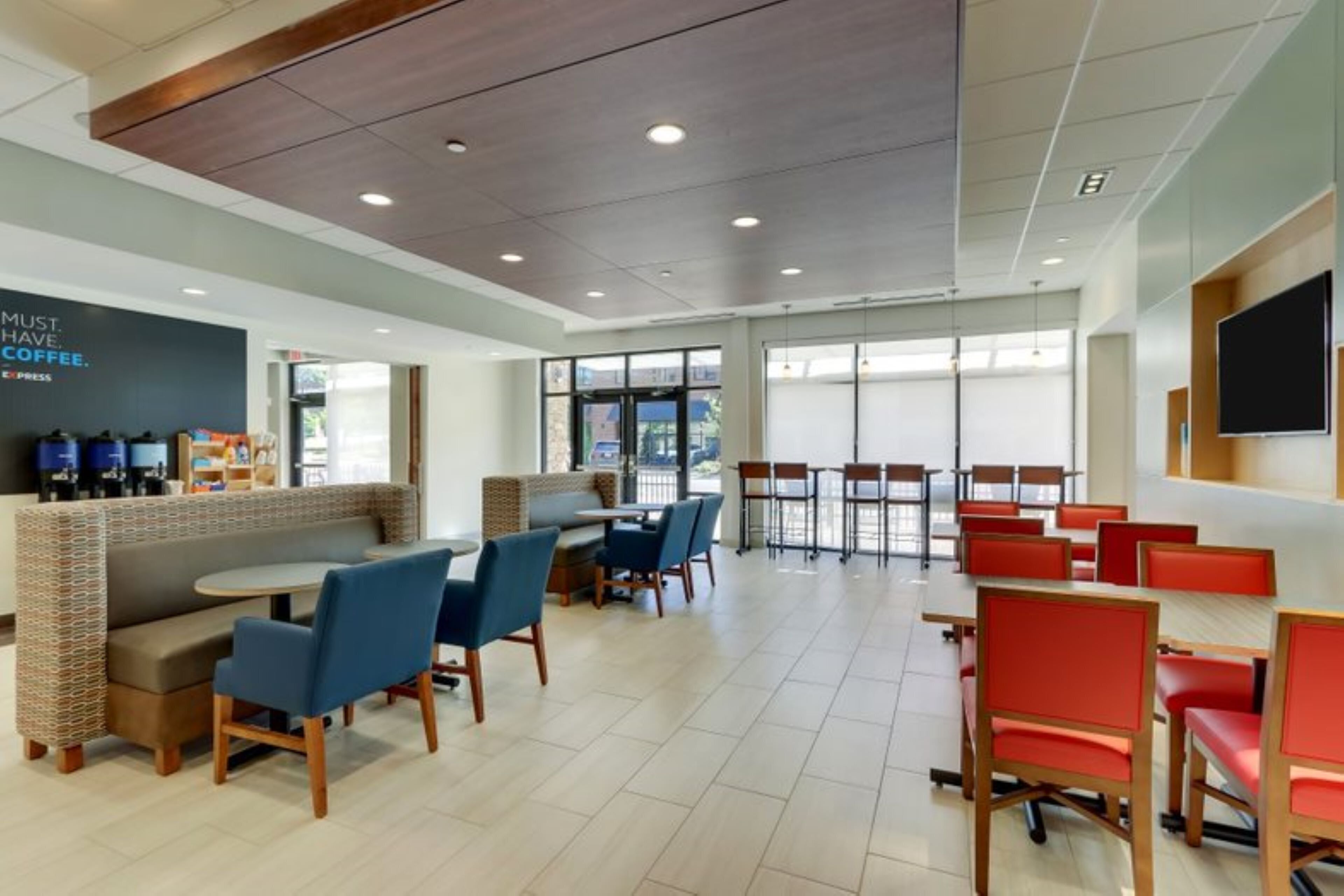 A modern indoor dining area with a seating arrangement that includes both booths and tables, a coffee station, and large windows providing natural light.