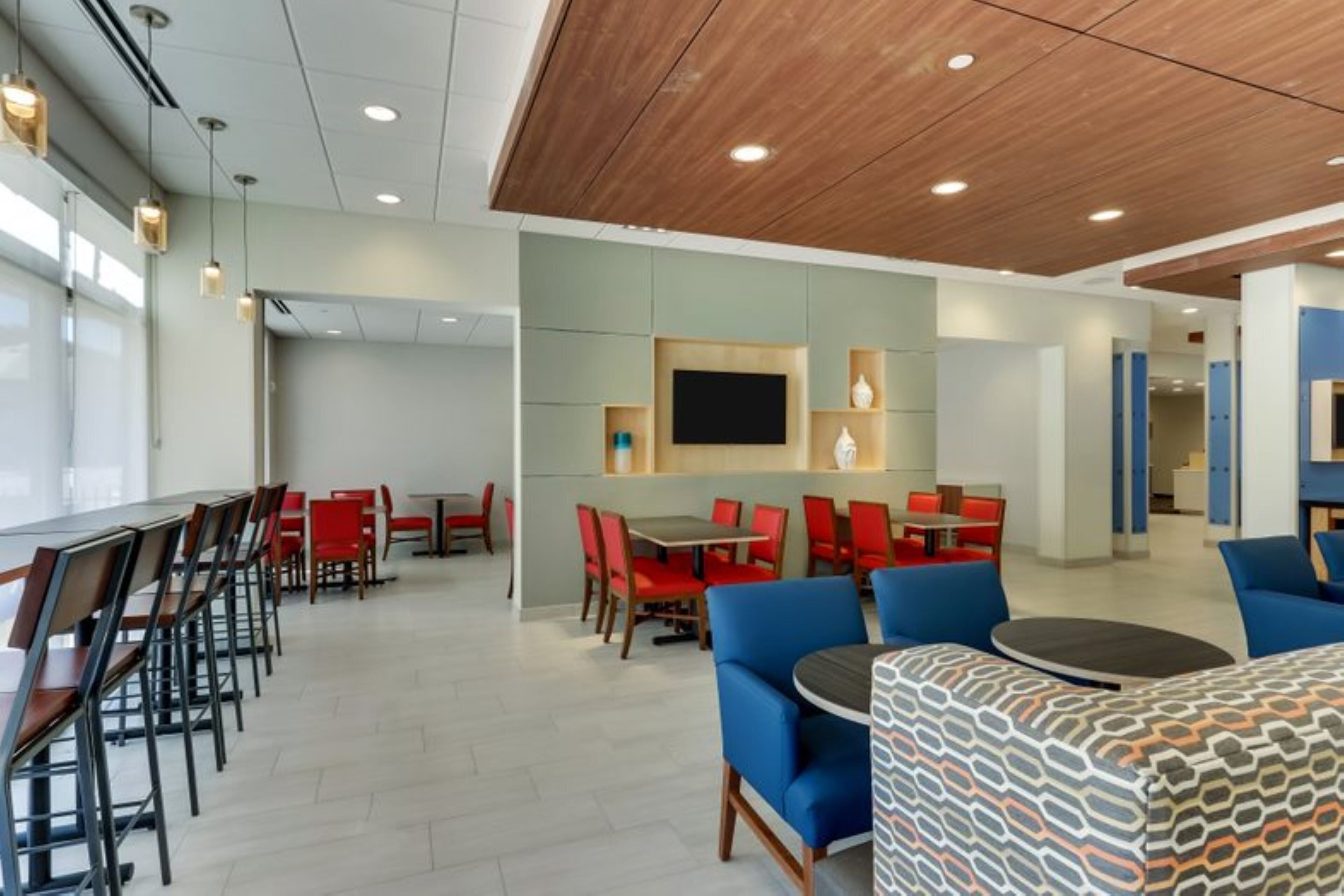 Un espace repas moderne avec des sièges rouges et bleus, un téléviseur à écran plat et un plafond en bois.