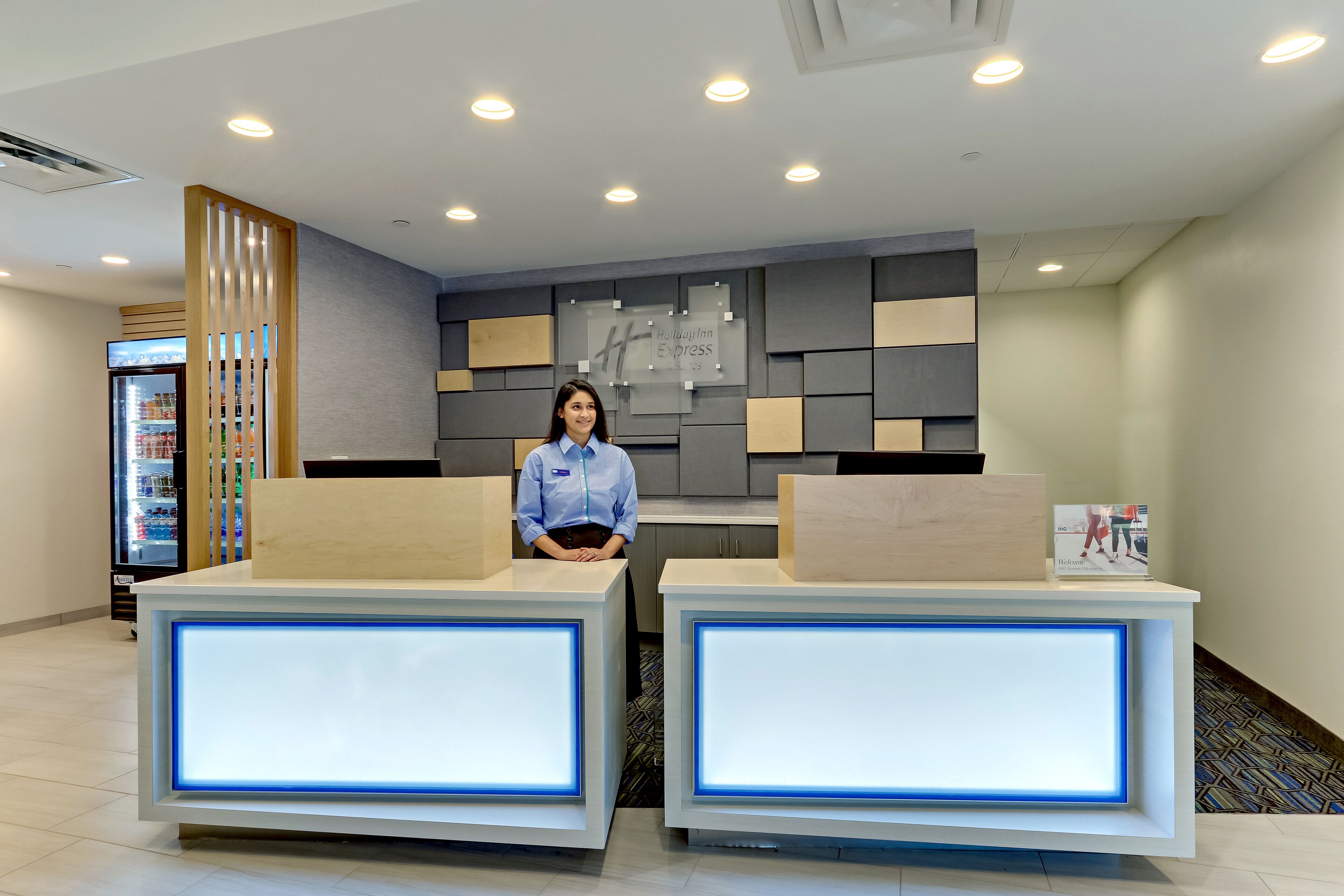 A hotel reception area with two reception desks, a refrigerator with beverages, and a wall-mounted sign.