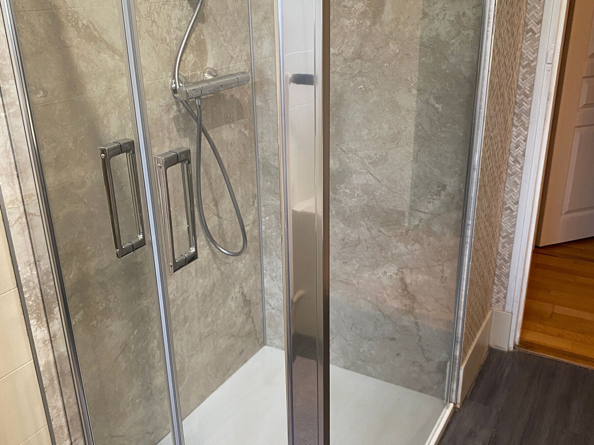Une douche fermée par des parois en verre, équipée d’un pommeau de douche à main et d’un pommeau de douche fixe.