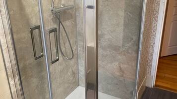Une douche fermée par des parois en verre, équipée d’un pommeau de douche à main et d’un pommeau de douche fixe.