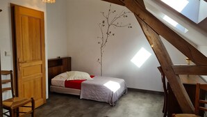 A bedroom with a sloped ceiling, a bed, a wooden chair, a small table, and a wall-mounted light fixture. - Farmhouse Retreat in Scenic Gâtinais - Spacious, Accessible & Eco-Friendly (Chailly-en-Gâtinais)