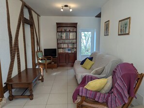 A living room with a sofa, a wooden chair, a bookshelf, and a television. - Farmhouse Retreat in Scenic Gâtinais - Spacious, Accessible & Eco-Friendly (Chailly-en-Gâtinais)