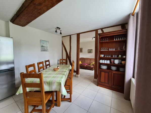 Un comedor con una mesa dispuesta para cuatro, sillas de madera, un aparador con vajilla y un cuadro en la pared.