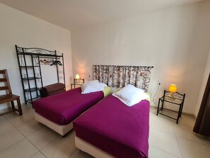 Een kamer met twee bedden, een metalen rek, een stoel en twee bedlampen.