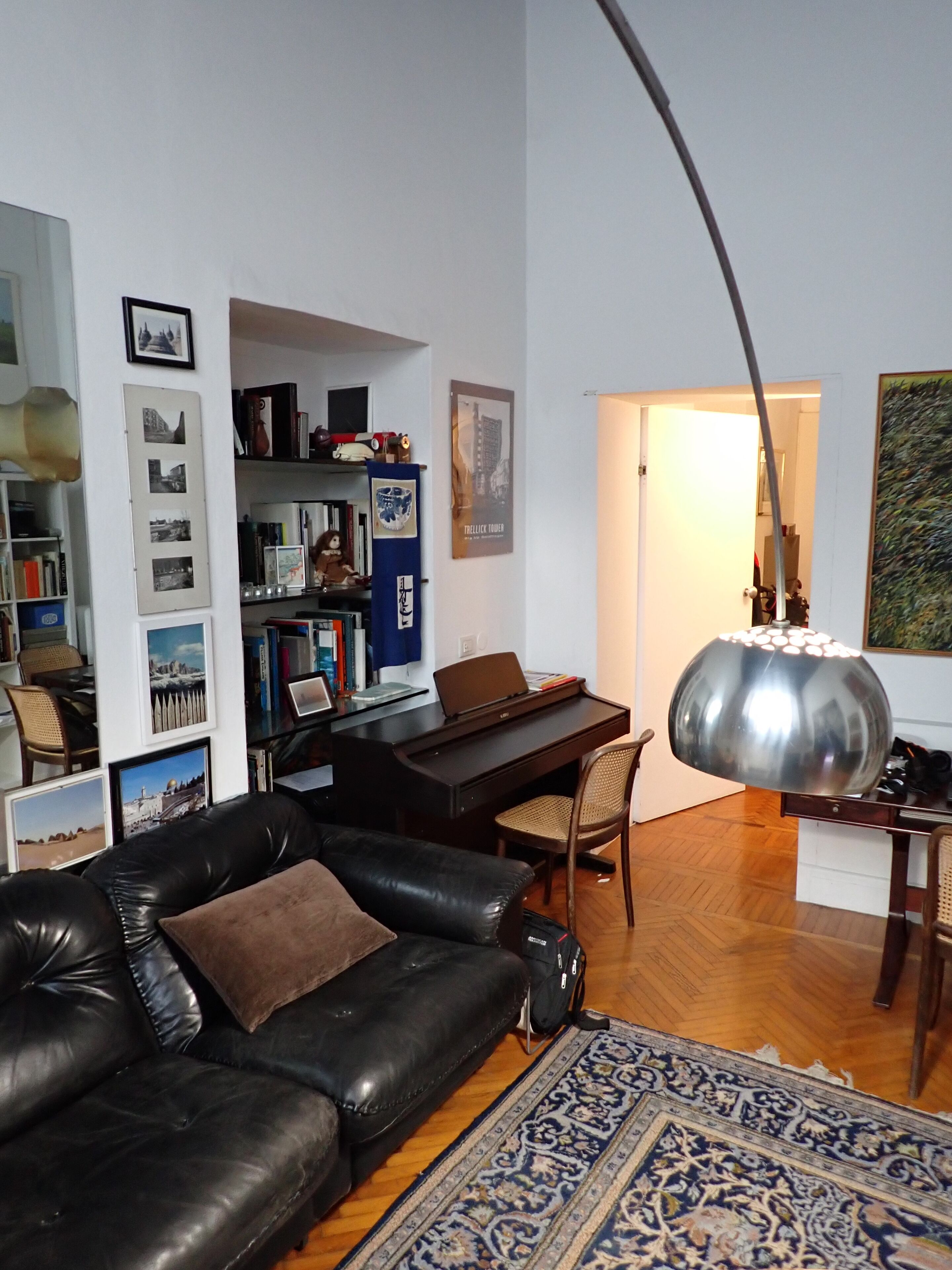 Een woonkamer met een zwarte leren bank, een piano, een boekenkast en een grote lamp.