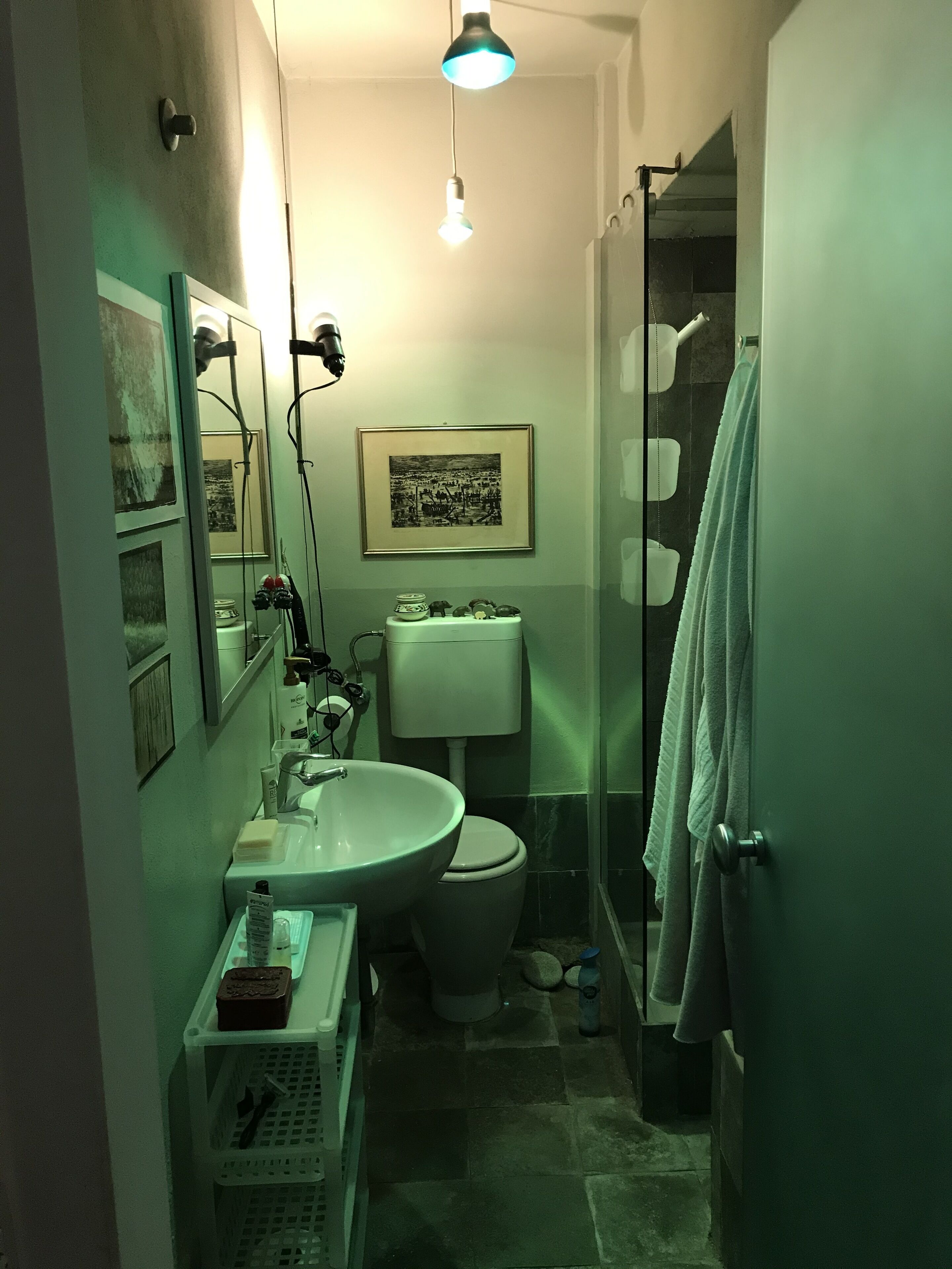 A compact bathroom with a sink, toilet, and shower. There are framed pictures on the wall and a light fixture above the sink.