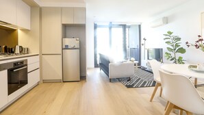 A modern kitchen with built-in appliances, a dining area with a table and chairs, and a sofa in the background.