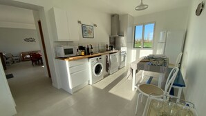 Cozinha moderna com micro-ondas, forno e máquina de lavar. Dispõe de área de refeições com mesa e cadeiras.