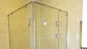 Une douche fermée par des parois de verre, dotée d’un pommeau de douche à main, d’une porte en verre et d’une barre d’appui.