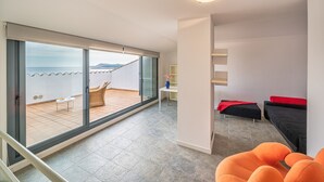 A modern room with a large sliding glass door leading to a balcony with a view of the sea. There is a sofa, a small table, and a chair inside the room. - Alba: Apartment on the seafront with views (L'Escala)