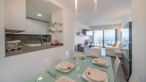 A modern kitchen with a dining area, white cabinets, and a large window. - Alba: Apartment on the seafront with views (L'Escala)