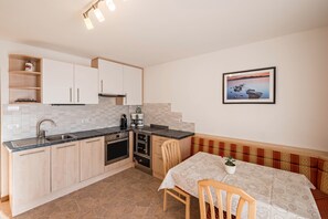 A compact kitchen with a sink, stove, and cabinets, a dining table with chairs, and a framed picture on the wall.