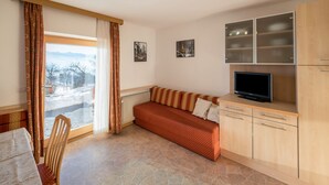 Um quarto aconchegante com sofá, televisão, armários e um espaço de refeições com mesa e cadeira.