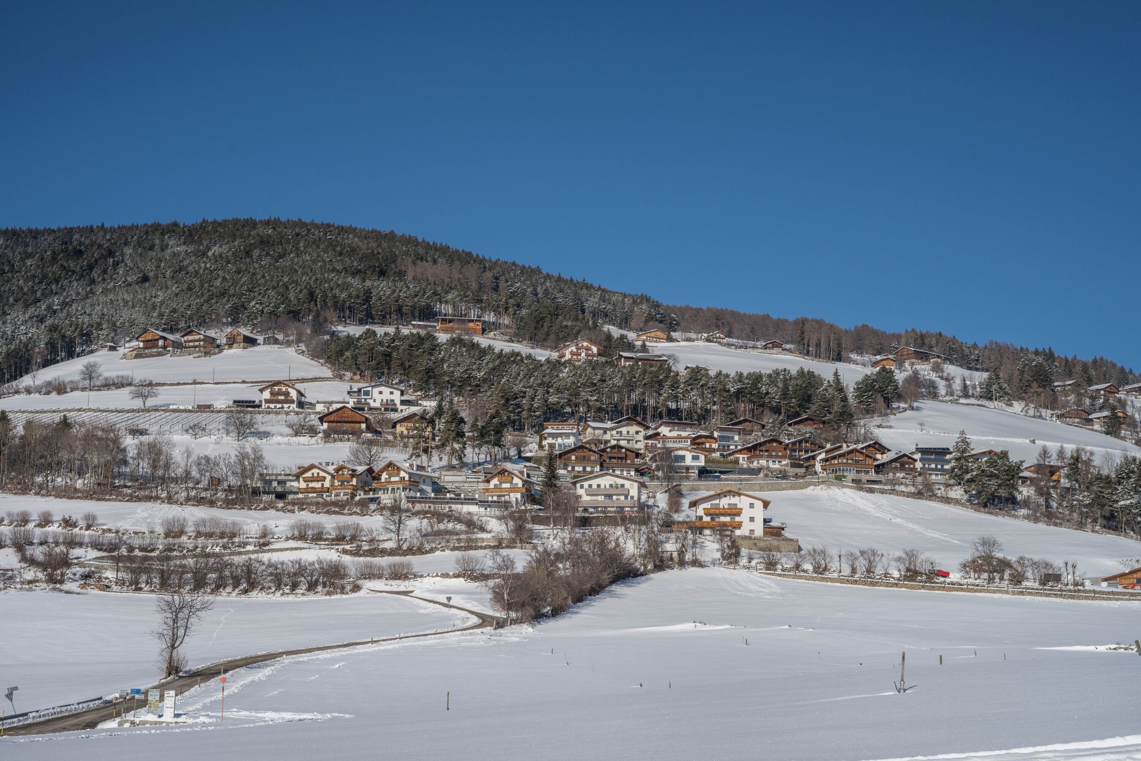 Un poble cobert de neu amb cases de fusta i un cel blau clar.