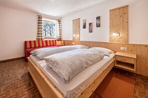 Un lit en bois avec une tête de lit rouge, une fenêtre avec des rideaux, des appliques murales et un parquet à motifs en chevrons.