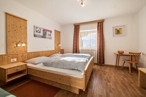 A wooden bed with a headboard, bedside tables, a small wooden desk, and a window with curtains.