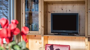 Puisesti sisustettu huone, jossa on televisio hyllyllä, lasikaapisto kirjoja varten ja punainen esine etualalla.