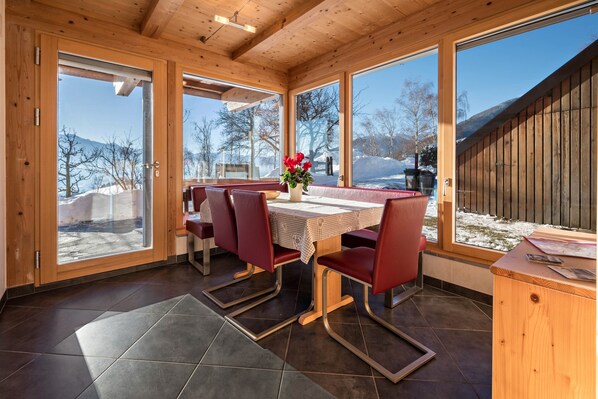 A wooden interior with a dining area, large windows, and a view of a snowy landscape.