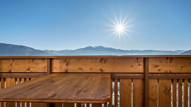 Une terrasse en bois avec une table et des bancs, d’où l’on peut admirer une chaîne de montagnes sous un ciel dégagé.