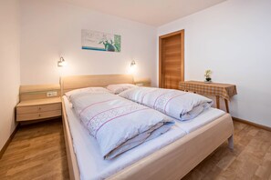 A bedroom with a bed, bedside tables, a nightstand, a small table with a plant, and a wooden door.