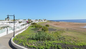 A coastal area with a paved walkway, a beach, and a row of white buildings with palm trees.