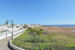 Eine Küstenlandschaft mit befestigtem Gehweg, Strand und einer Reihe weißer Gebäude mit Palmen.