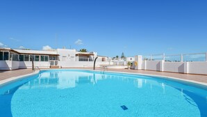 A clear blue swimming pool surrounded by white buildings with large windows and balconies.