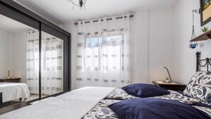A bedroom with a bed, a nightstand, a mirror, and a window with curtains. - Holiday Home ‘Finca Alejandrina’ with Sea View, Pool, Garden & Wi-Fi (La Guancha)