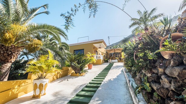 A pathway leading to a yellow building with a staircase, surrounded by palm trees and potted plants. - Holiday Home ‘Finca Alejandrina’ with Sea View, Pool, Garden & Wi-Fi (La Guancha)
