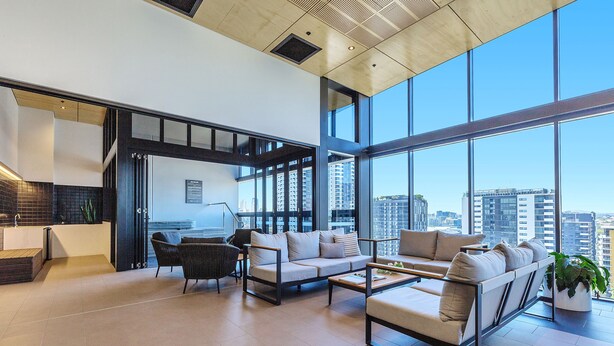 A spacious living area with a large window, a sofa set, a coffee table, and a kitchen area with a sink and countertop. - KOZYGURU BRISBANE ONE 1Bed APT Parking (South Brisbane)