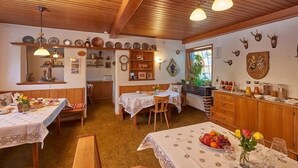 A cozy dining area with wooden beams, a central table with a fruit bowl, and a window with a view of greenery. - Comfortable three-room vacation apartment with kitchen and south-facing balcony (Reit im Winkl)