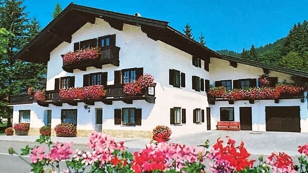 A two-story building with balconies, flower boxes, and a red bench. - Comfortable three-room vacation apartment with kitchen and south-facing balcony (Reit im Winkl)